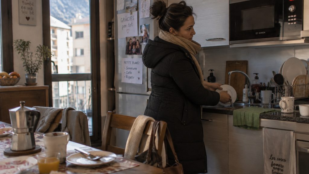 Mujer fregando los platos del desayuno con el abrigo puesto en un piso de Sant Julia de Loria