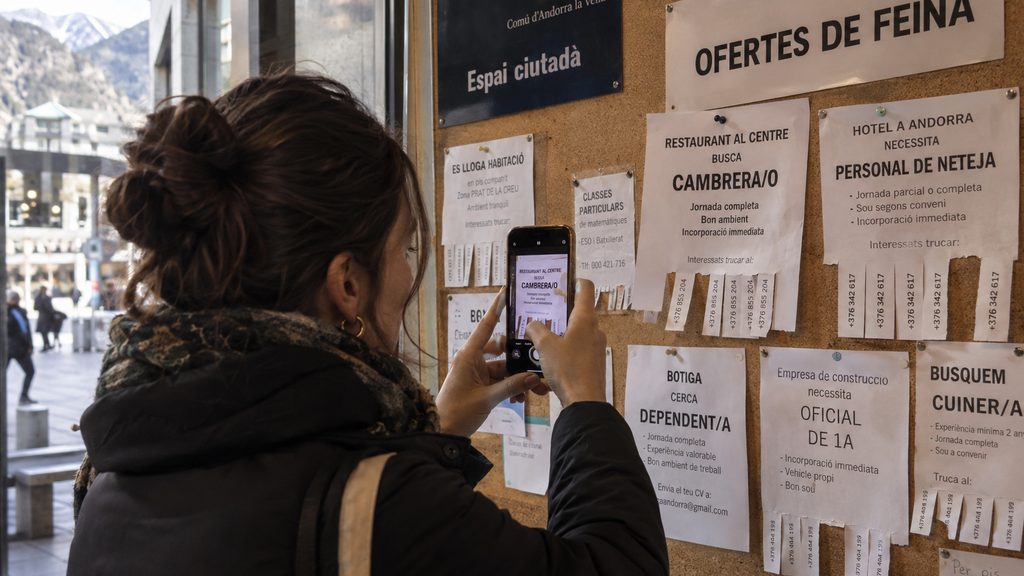 Mujer fotografiando con el móvil una oferta de trabajo en un tablón de anuncios en Andorra
