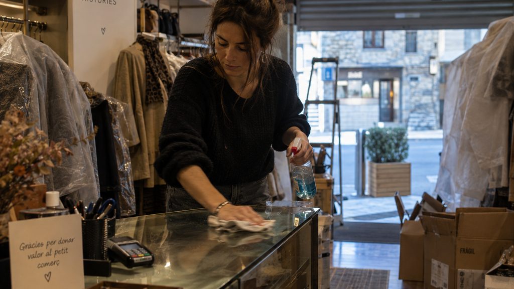 Mujer limpiando el mostrador de una tienda de Andorra con la persiana a medio subir antes de abrir