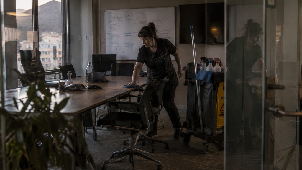 Limpiadora repasando la mesa de una sala de reuniones en una oficina de Andorra al acabar el día